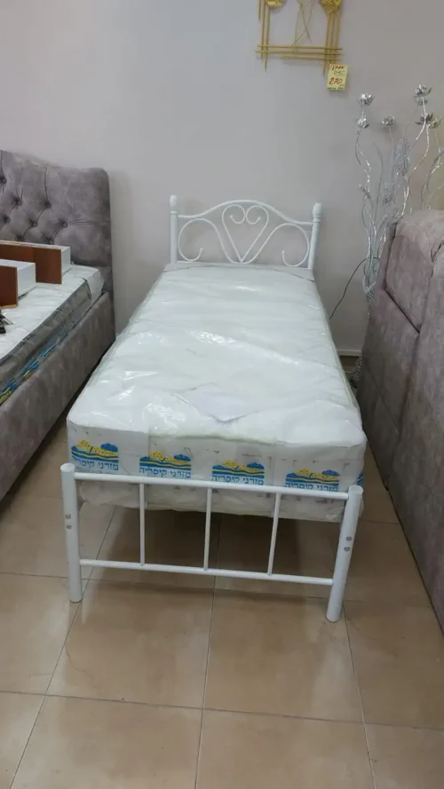 מיטה קטנה עם מסגרת לבנה, חלק מחדר שינה עם רהיטים רכים ומעבר לעיצוב מודרני.
